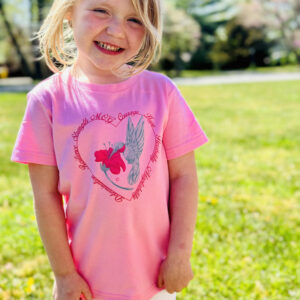 Mya shows off the Hummingbird shirt: she has blonde hair and is wearing a pink short sleeved t-shirt with our hummingbird and heart design.