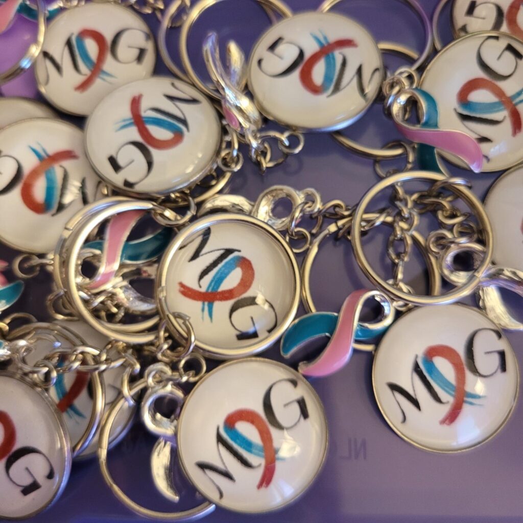MOG Pins made by Dana Yates: they have the letters MOG with a teal and ruby rose ribbon as the O.