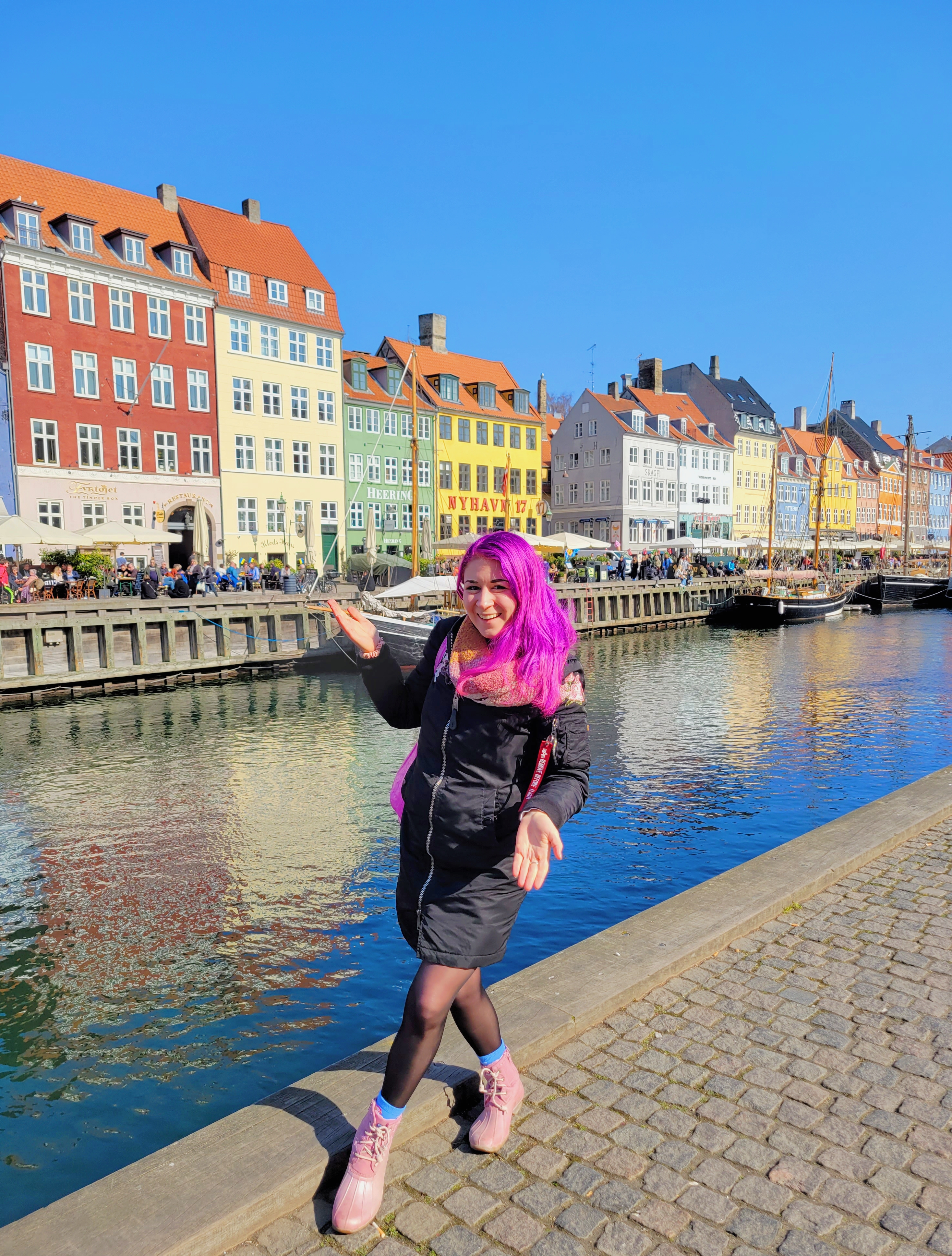 Danielle Silverman with pink hair in front of a canal with colorful houses in the background - possibly Amsterdam
