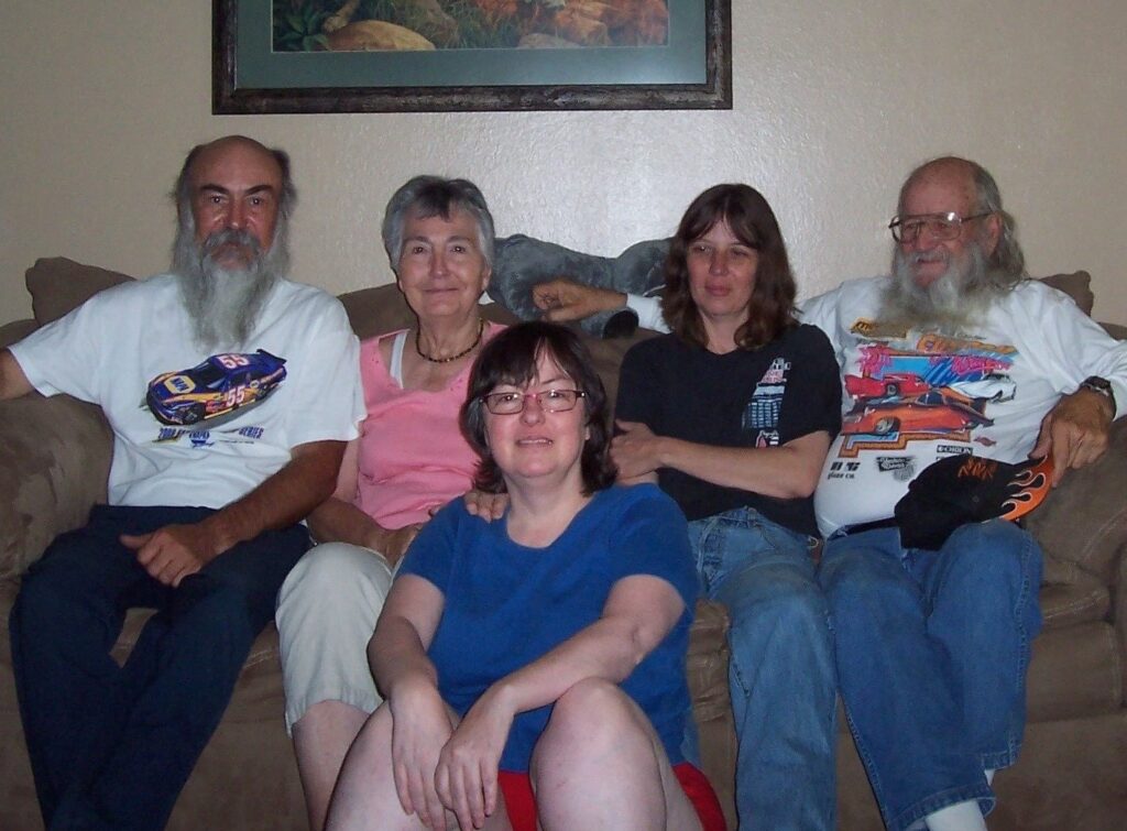 Staged on a light brown couch against a tan wall where a painting is hanging above them, Kandias is seated on the floor facing the camera. She is leaning back on the couch where her brother, Gary, her mom, Myrtle, her sister, Molly, and her dad, Bill are seated.