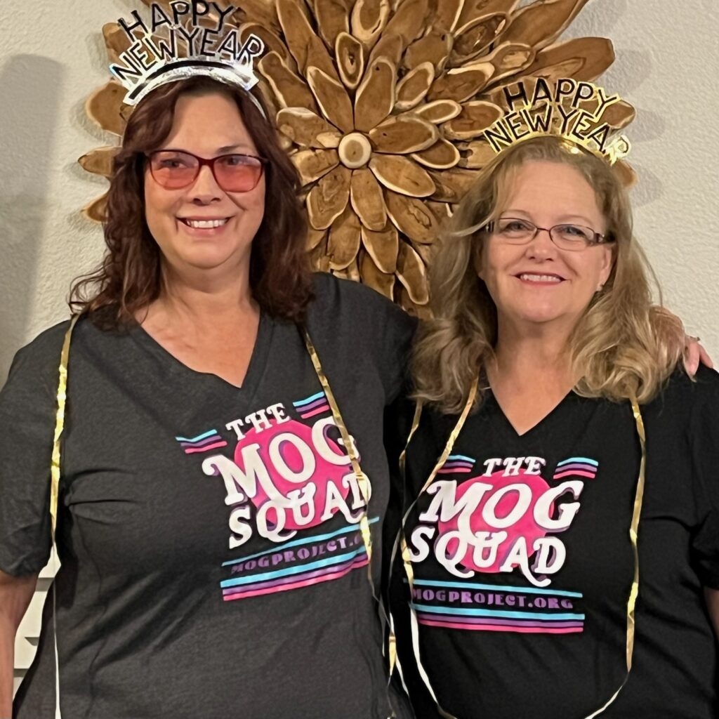 Dana is standing with Andrea wearing their best smiles with MOG SQUAD t-shirts, shiny New Years crowns and gold streamers around their necks.