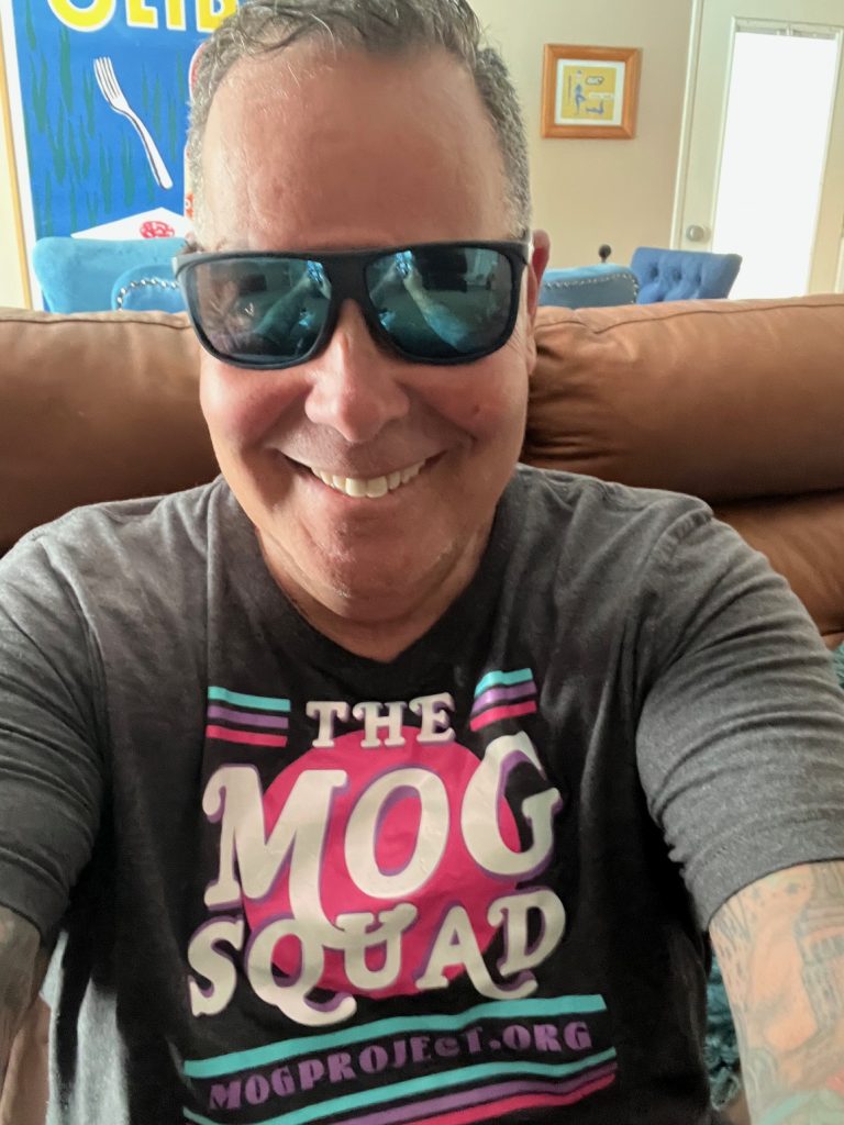 Jim is smiling, in sunglasses and wearing a shirt that says The MOG Squad, mogproject.org.