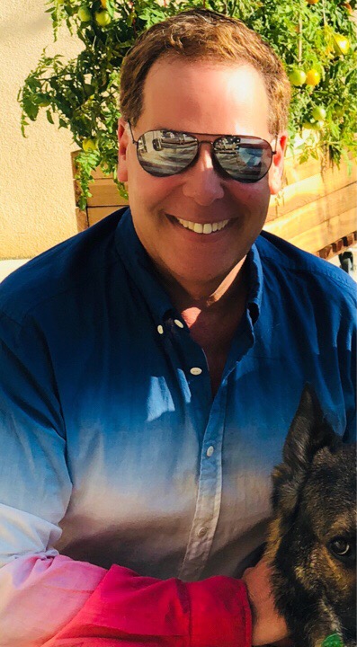 Jim Smiling and wearing sunglasses and a blue rainboow gradient shirt.