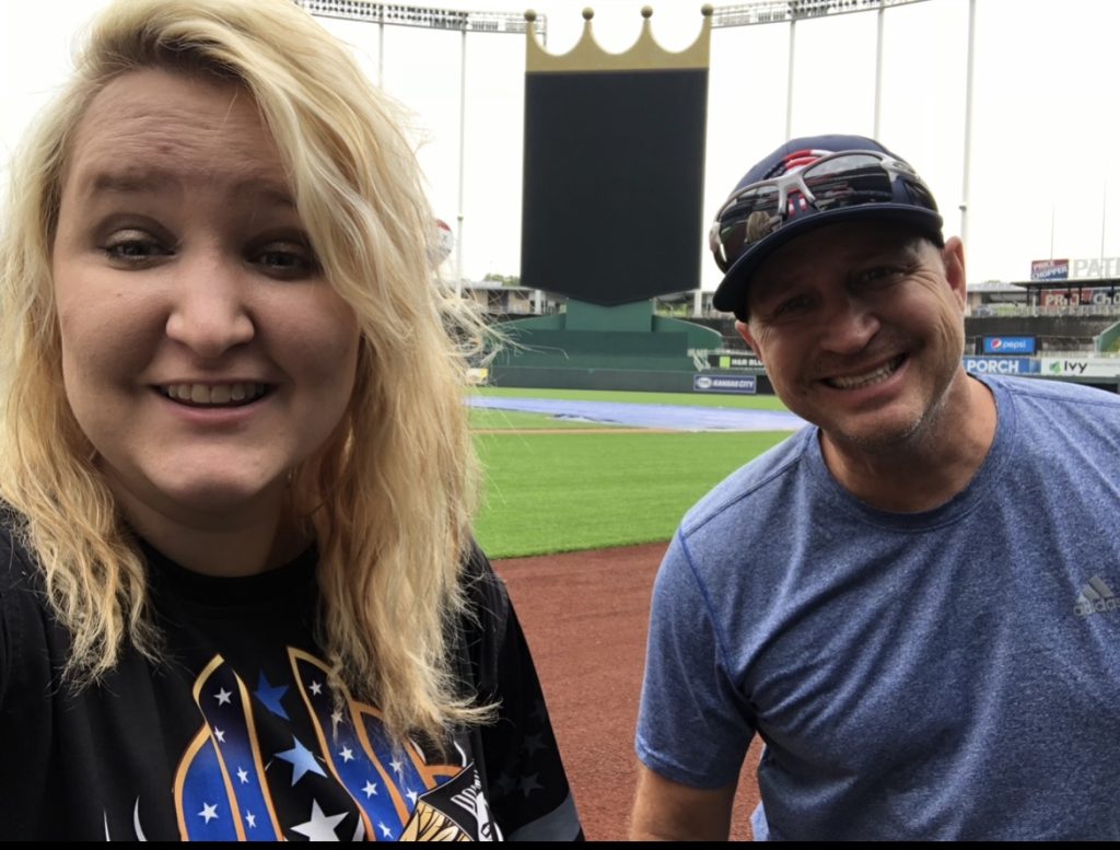 Alexandra is smiling at the camera. The background is of a baseball stadium.