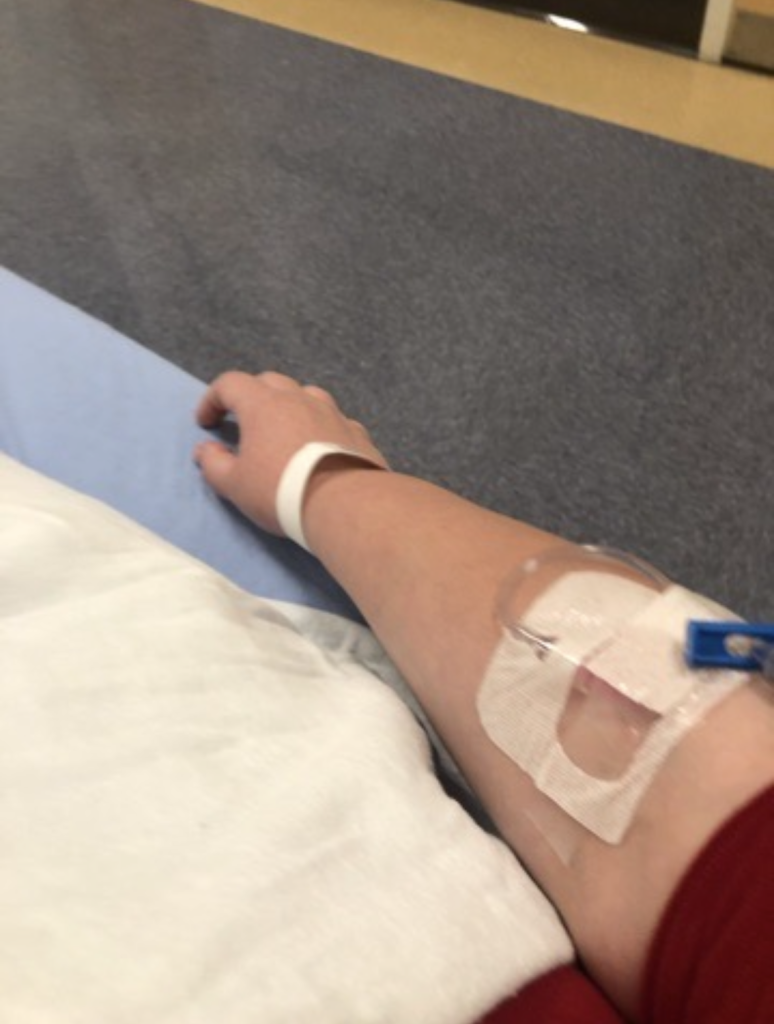 Alexandra's arm which is connected to an IV. She appears to be at an infusion center.