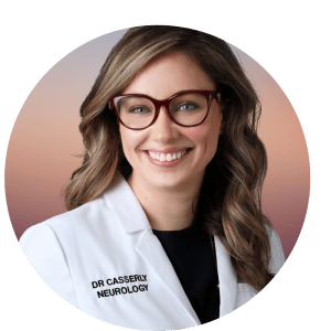 Courtney Casserly, MD, FRCPC is shown with a white lab coat on, a dark shirt underneath, long blonde hair and dark glasses. She is smiling.