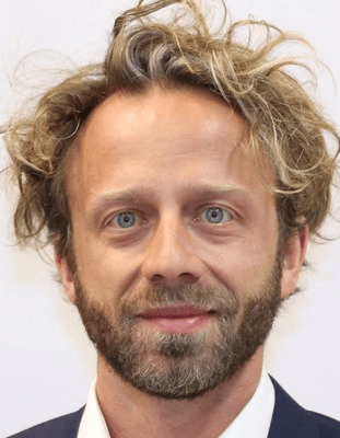 Enrico is shown with dark blonde hair and a beard. He is smiling.