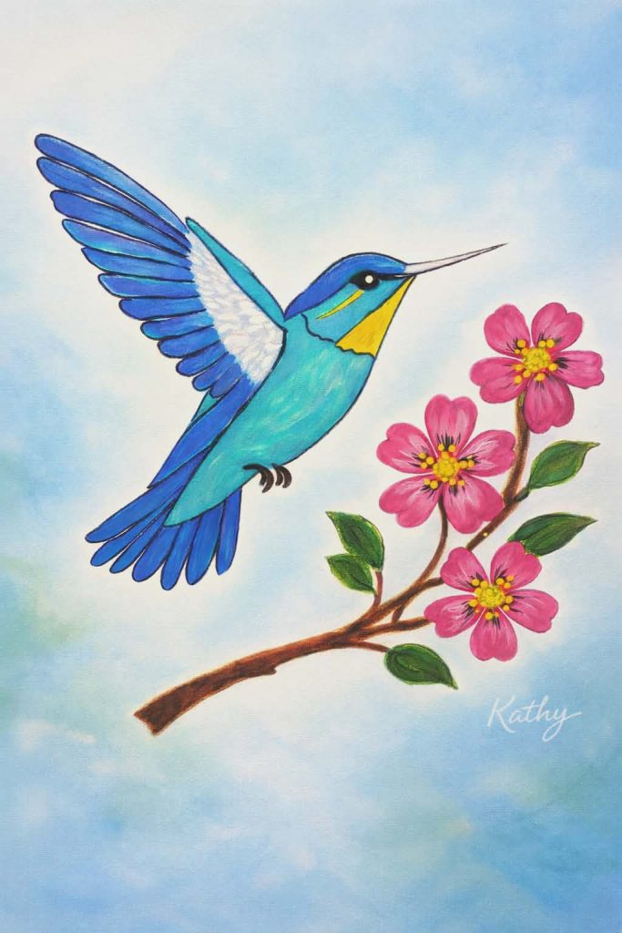 A colorful illustration for MOGAD Awareness Month shows a blue and yellow hummingbird hovering beside a branch with pink flowers and green leaves, set against a light blue sky. The artist’s signature, Kathy, appears at the bottom right.