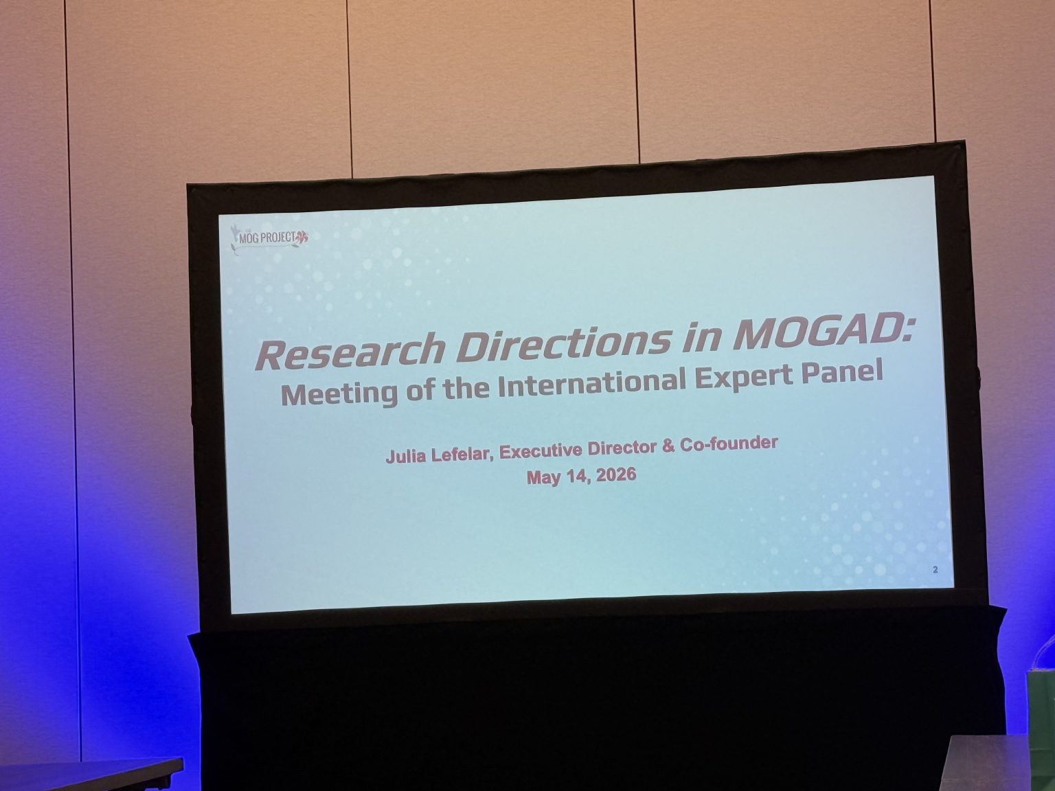 A presentation screen displays the title Research Directions in MOGAD: Meeting of the International Expert Panel by Julia Lefelar, Executive Director & Co-founder, dated May 14, 2026.