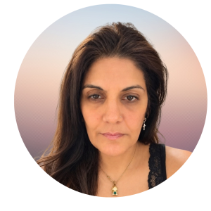 Pooja with long brown hair, wearing a black lace top, a cross earring, and a necklace, gazes neutrally at the camera. Background is a gradient of soft pink and blue tones—About The MOG Project.